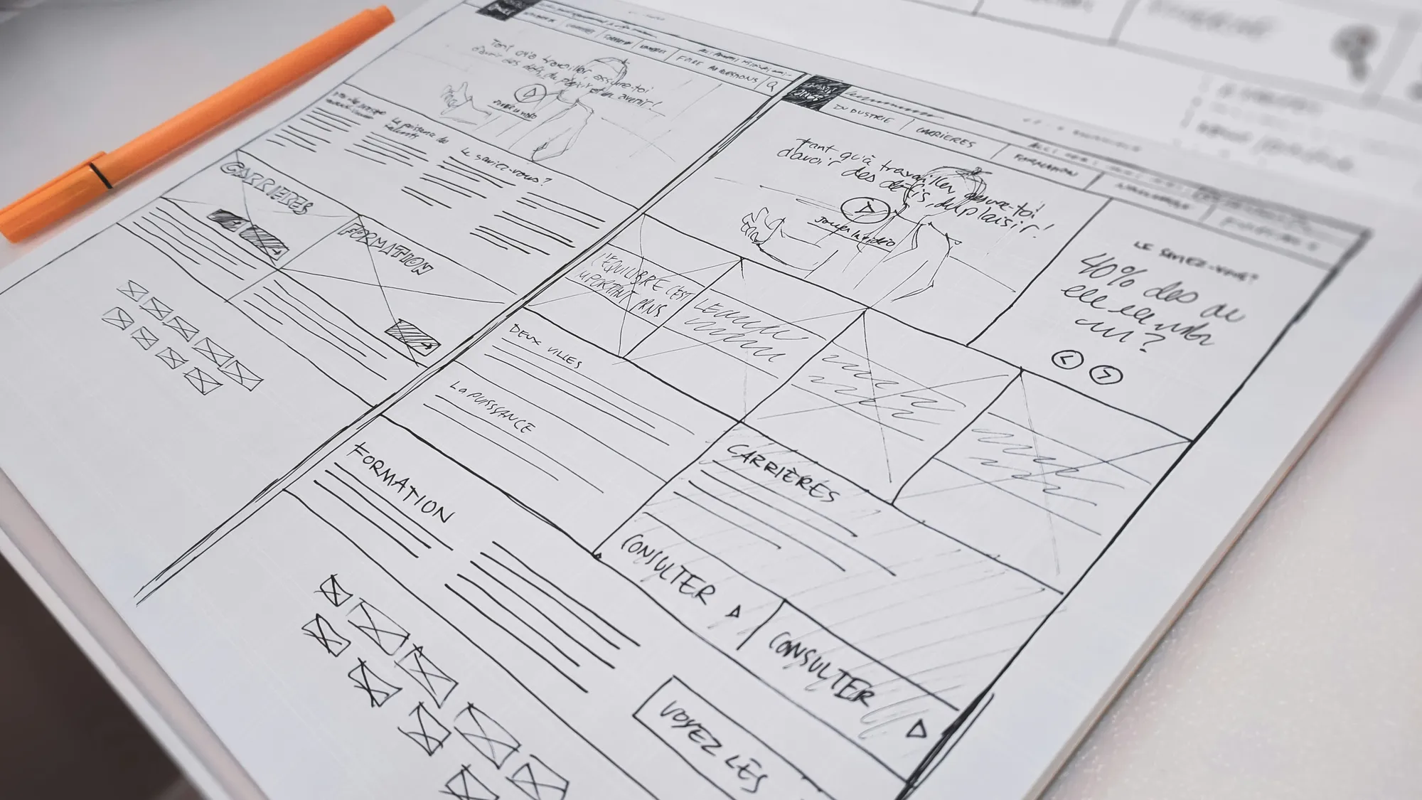 Hand-drawn website wireframes comparing page layouts on paper beside an orange pen.