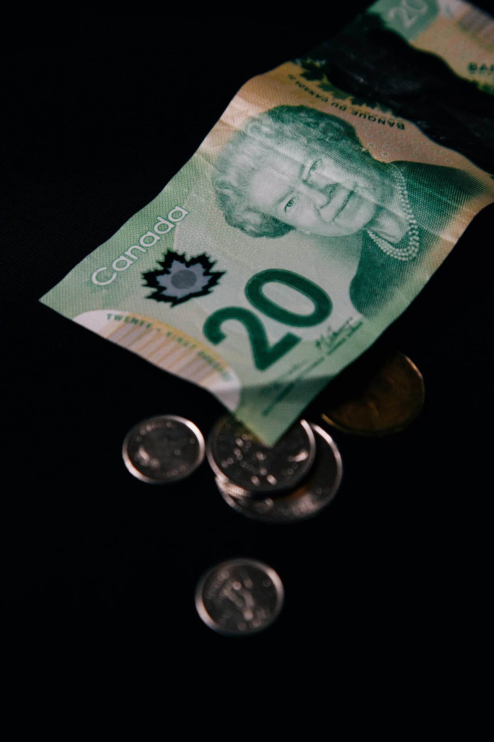 A Canadian 20-dollar bill and several coins scattered on a black background, representing budgeting and website design cost Toronto.