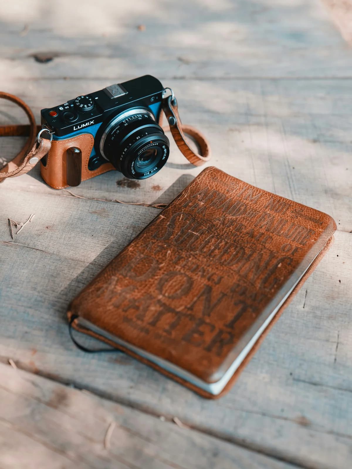 A film camera and a debossed leather journal resting on weathered wood, the slow editorial tools behind the section-first writing discipline that passage optimization rewards.