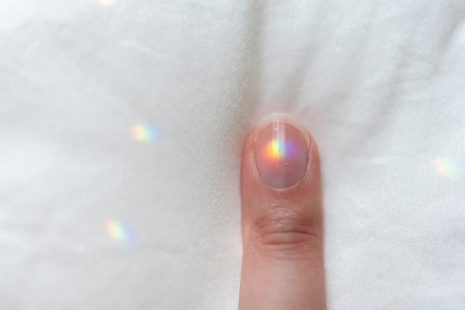 A close up shot of a person pointing a single finger against a clean white fabric background with tiny rainbow light reflections catching on the fingernail, symbolizing focusing in on the top priority item from a website audit checklist.