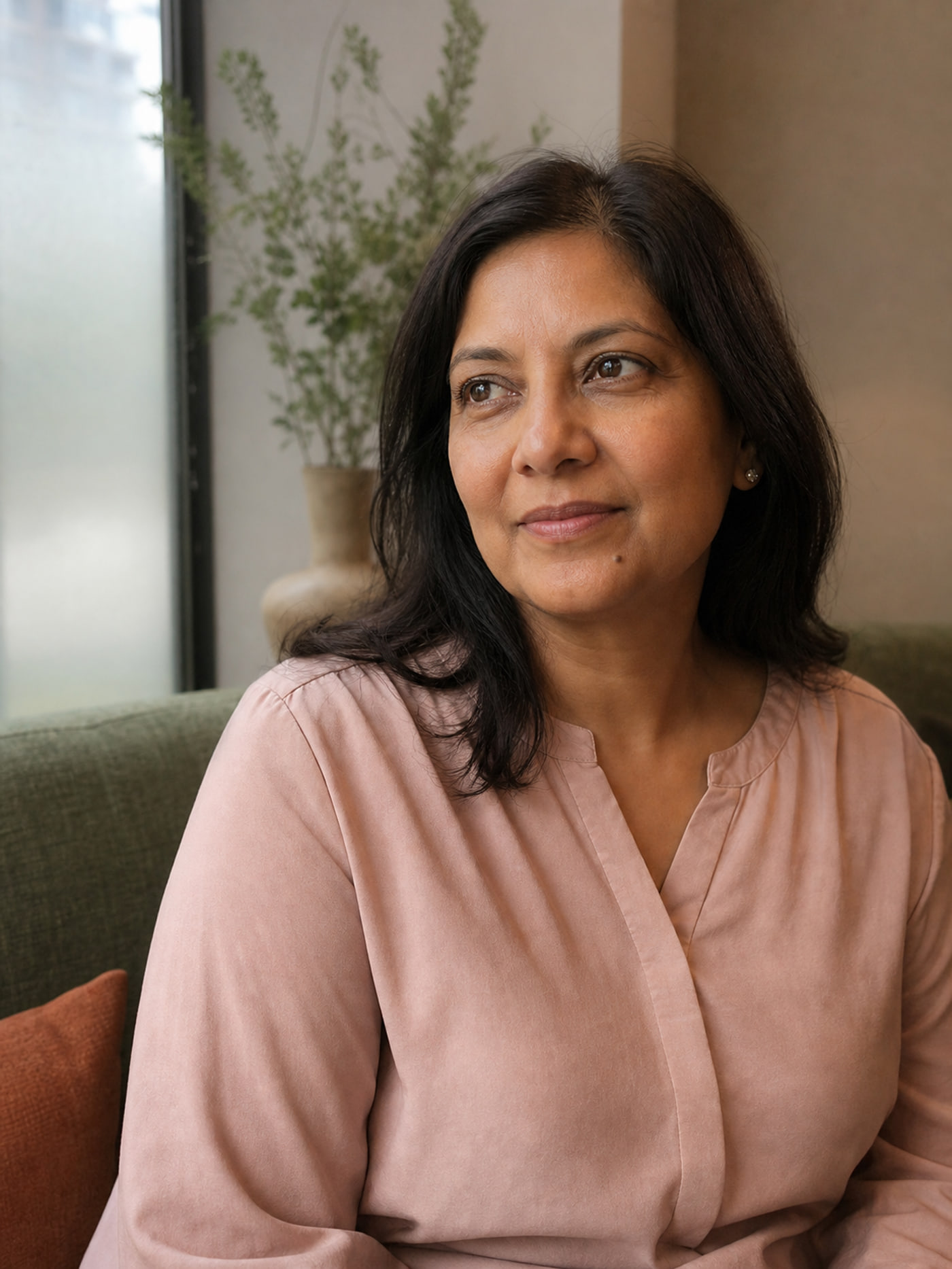 Priya, a fictional LumaSkin client, seated by a studio window