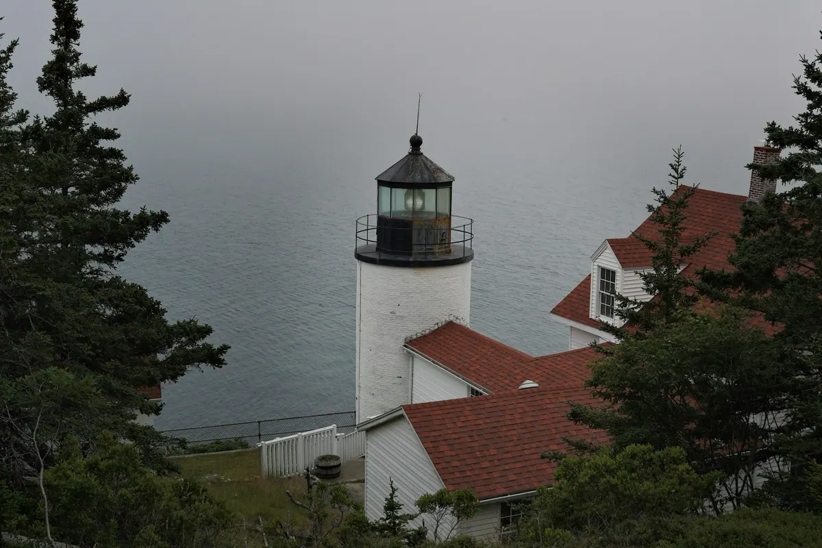 A foggy coastal lighthouse with red-roofed buildings
